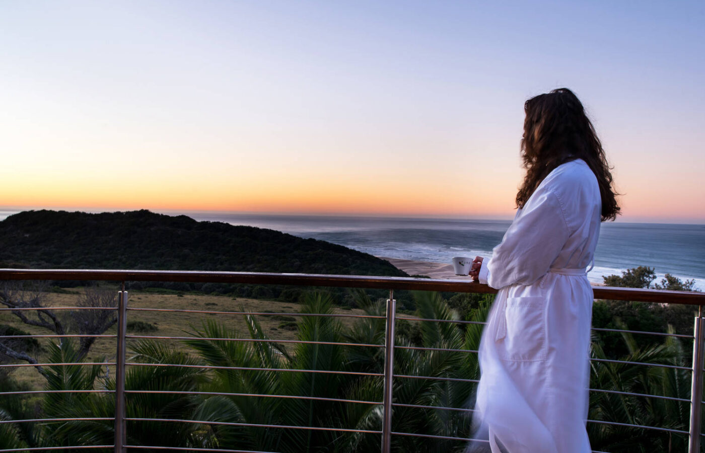 S008 - IT2 - Woman in White Bath Robe Overlooking the View from the Balcony Sustainable Safaris Africa - Journeys - Luxury Eastern Cape Couples Safari - Woman in White Bath Robe Overlooking the View from the Balcony